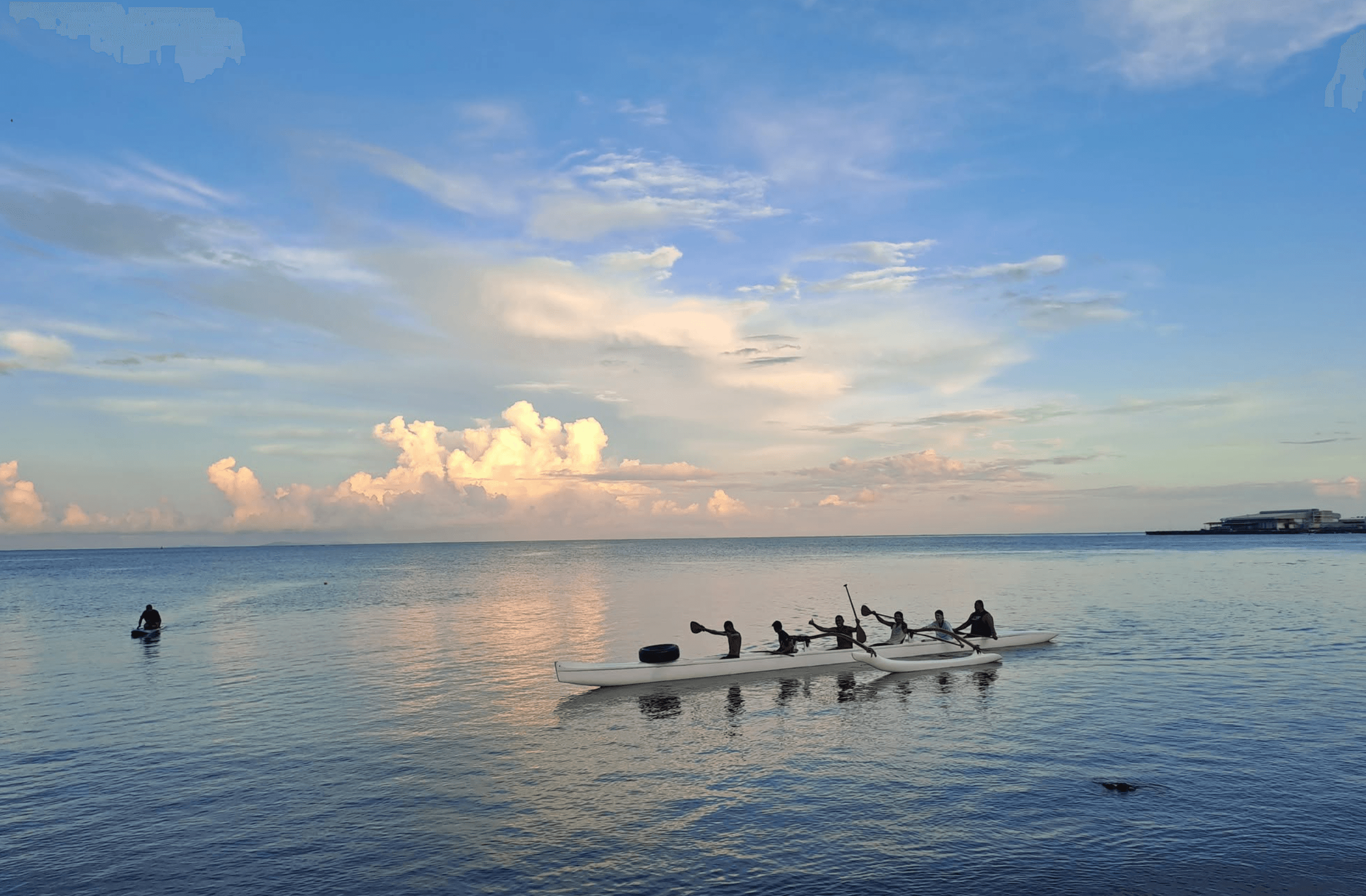 OOCSA paddlers returning across calm water beneath a colorful Fiji sunset